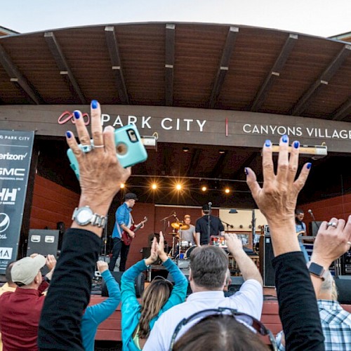 People enjoying a live concert at Park City's Canyons Village, hands raised and phones out to capture the moment.