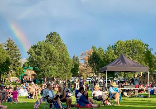 People are gathered in a park with lawn chairs, a canopy, and a rainbow in the sky visible in the background.