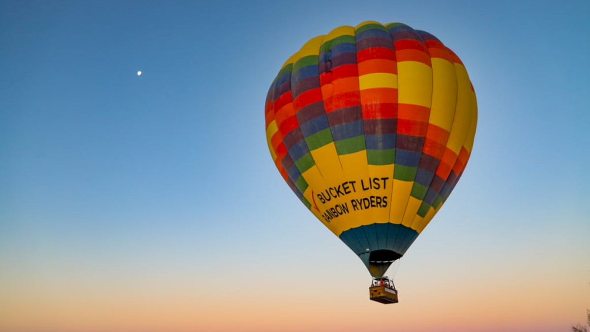 The image shows a colorful hot air balloon with a basket beneath, floating against a clear sky during sunset.