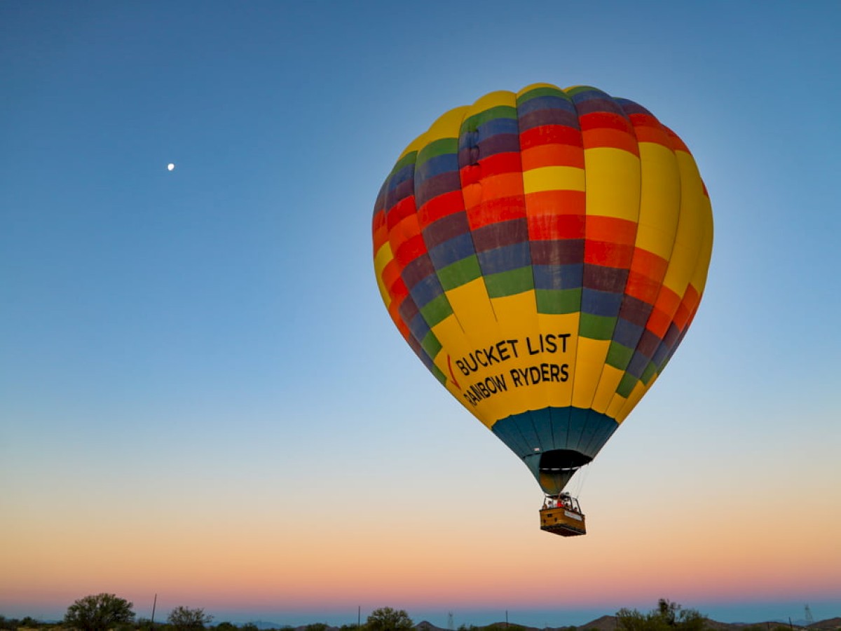 The image shows a colorful hot air balloon with a basket beneath, floating against a clear sky during sunset.