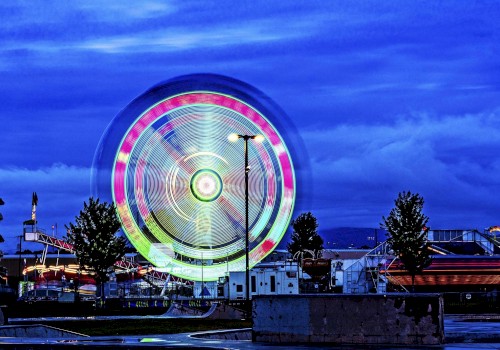 A brightly lit amusement park at night with a spinning Ferris wheel, other rides, and trees under a dark blue sky ending the sentence.