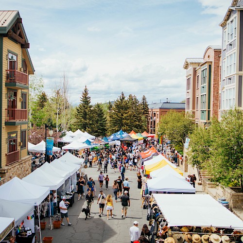 a photo of downtown park city on the day of the park sill sunday market. tents are put up of people selling goods with families walking around the area at different booths