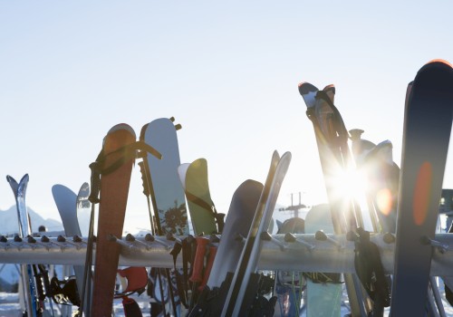 The image shows a row of skis and snowboards standing upright in the snow with the sun shining in the background.