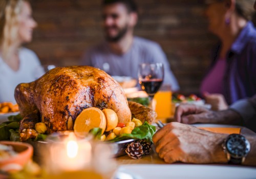 A roasted turkey garnished with oranges is on a table surrounded by people enjoying a meal together, with wine and candles present.