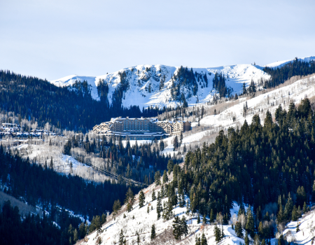 A snowy mountain landscape with a large resort nestled among trees, surrounded by snow-covered peaks and forested hillsides.