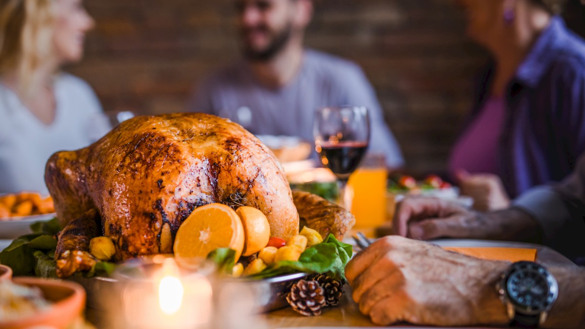 A roast turkey centerpiece with oranges and vegetables, surrounded by people enjoying a meal, creating a warm, festive atmosphere.