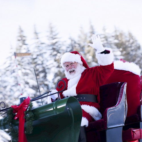 Santa Claus is sitting in a sleigh, waving, with a snowy forest in the background.