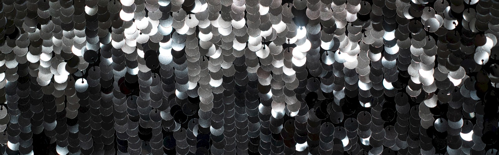 The image shows a close-up of numerous reflective sequins or circles creating a shimmering, abstract pattern in black and white tones.