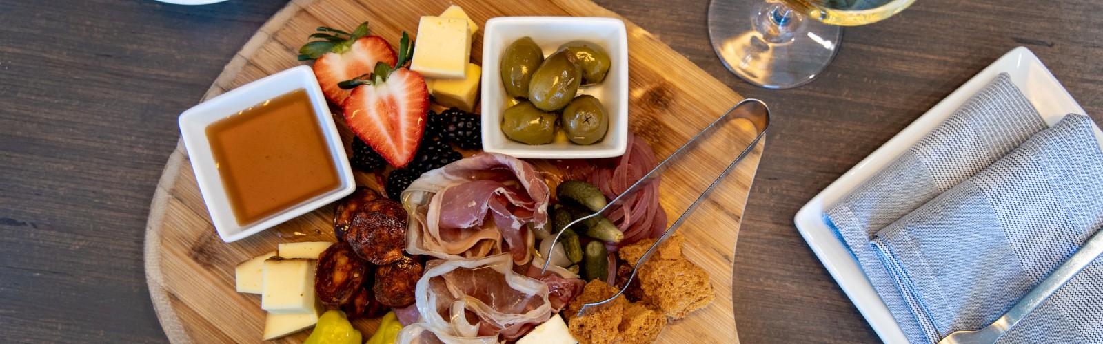 A charcuterie board with meats, cheeses, olives, and fruit; accompanied by bread and a glass of white wine.