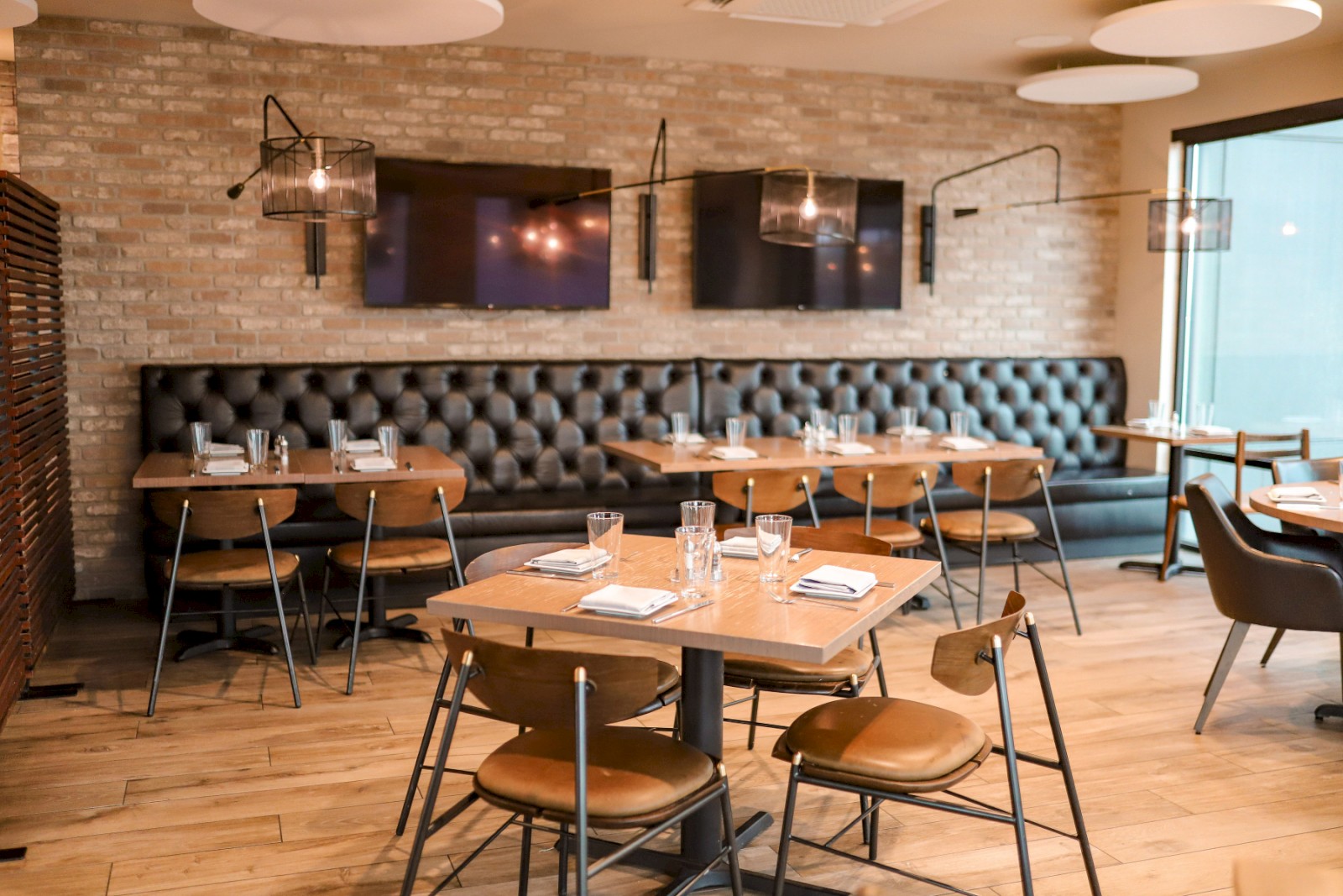 The image shows a modern restaurant interior with wooden tables, leather chairs, and soft lighting, creating a cozy dining atmosphere.