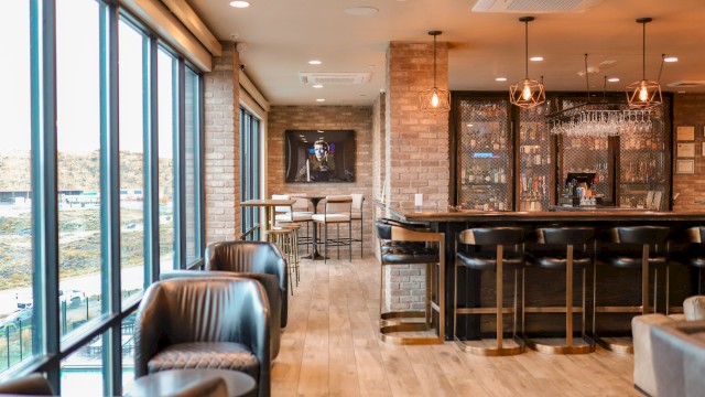 A modern lounge with large windows, leather seating, a bar counter, and hanging lights, featuring a warm and inviting atmosphere.