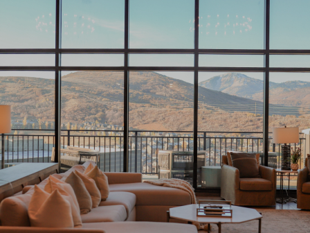 A cozy living room with large windows showcases a mountain view, furnished with couches, chairs, and a table with books.