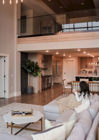 A bright, modern open-plan living area with a white sofa, high ceilings, a kitchenette, and a balcony railing on the upper level, cozy and stylish.