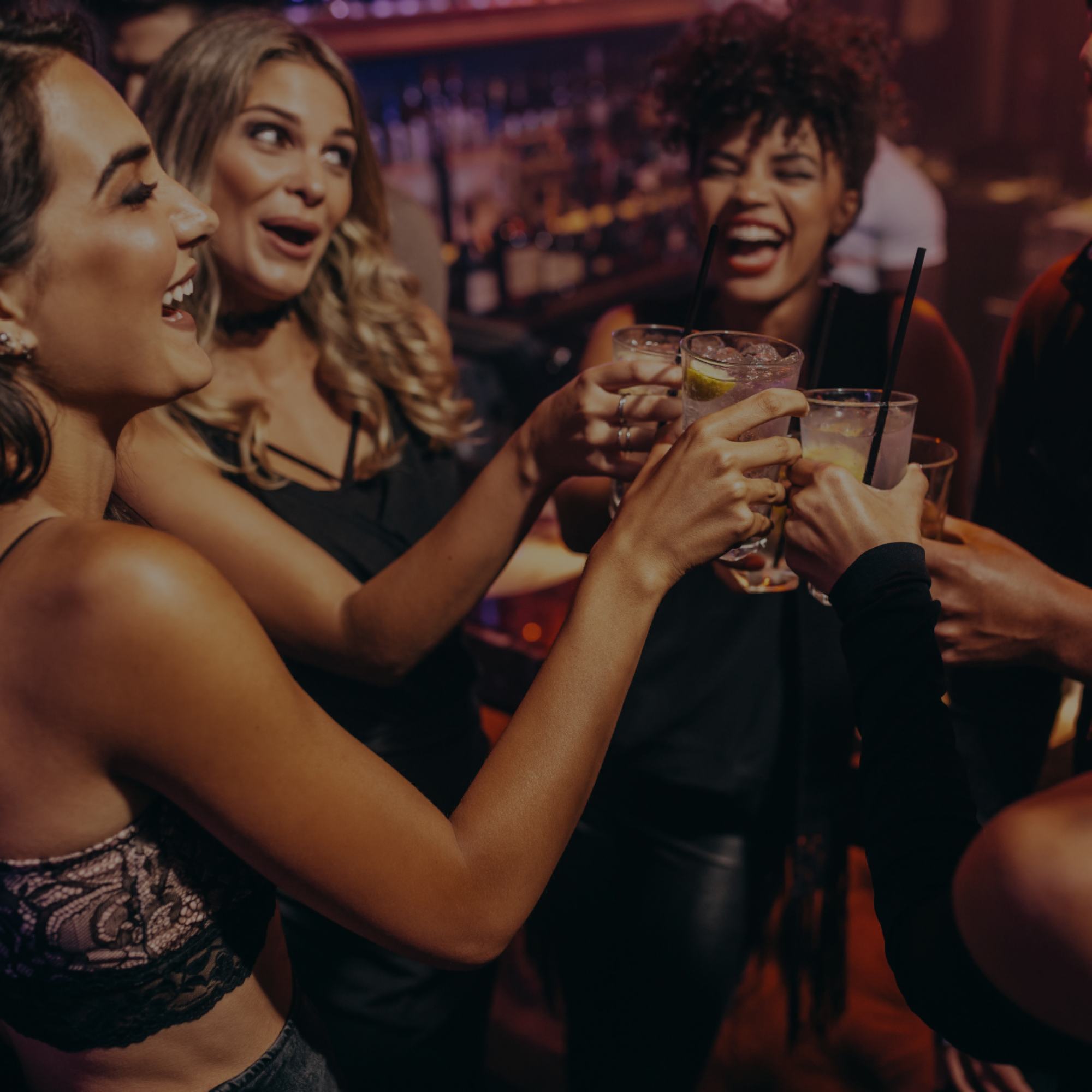 A group of people are joyfully toasting with drinks in a lively bar setting.