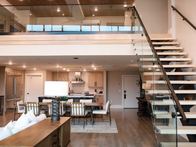 The image depicts a modern, open-concept living space with a kitchen, dining area, and a staircase leading to an upper floor.