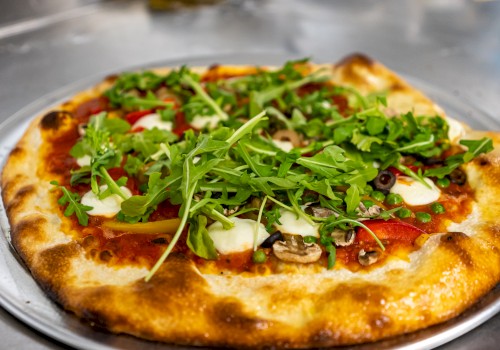 A pizza topped with arugula, cheese, olives, mushrooms, and peppers on a metal tray.