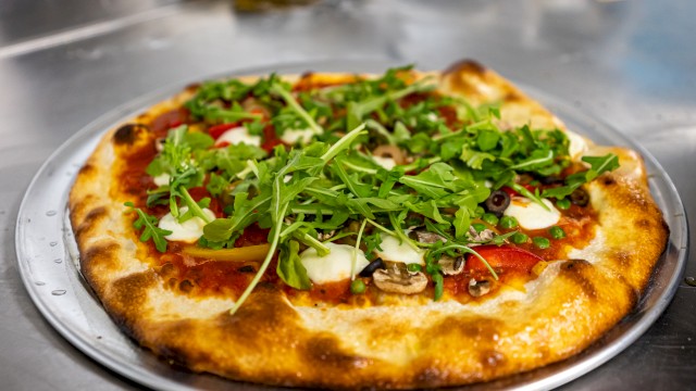A pizza topped with arugula, cheese, olives, mushrooms, and peppers on a metal tray.