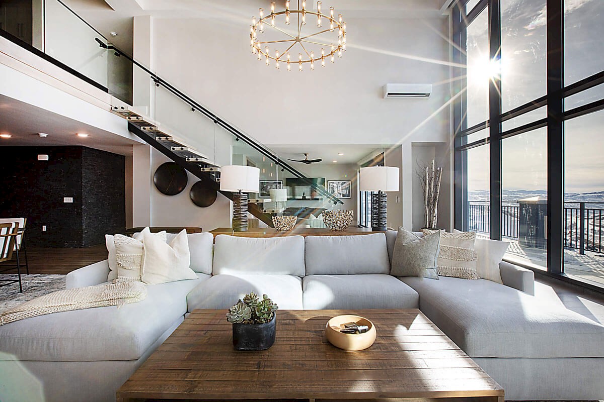 A spacious, modern living room with a sectional sofa, large windows, wooden table, and a view of a staircase.