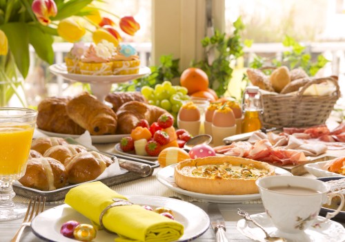 A lavish breakfast spread with pastries, fruit, eggs, quiche, juice, and coffee on a table adorned with a floral centerpiece.