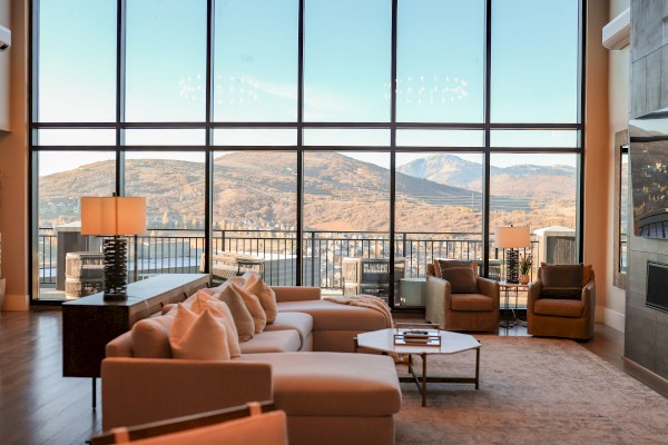 A cozy living room with plush seating, large windows showcasing a scenic mountain view, and ambient lighting from lamps.