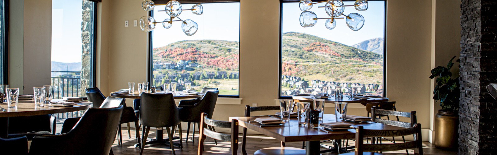 A modern, sunlit restaurant with elegant decor and panoramic mountain views through large windows.