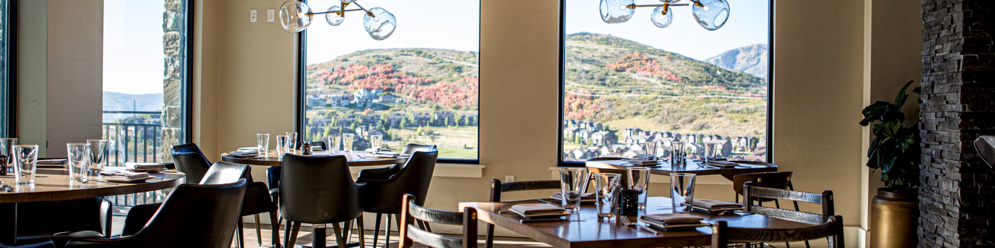 A modern, sunlit restaurant with elegant decor and panoramic mountain views through large windows.