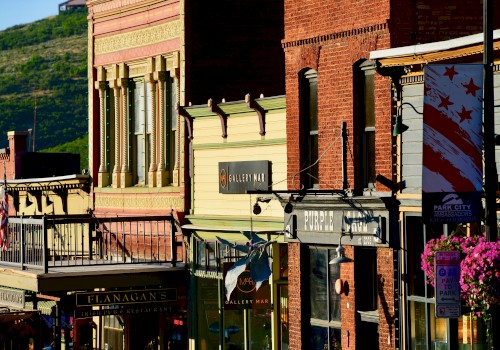 A colorful street with historic buildings, various store signs, and a decorative flag. Bright sunlight highlights the architectural details.