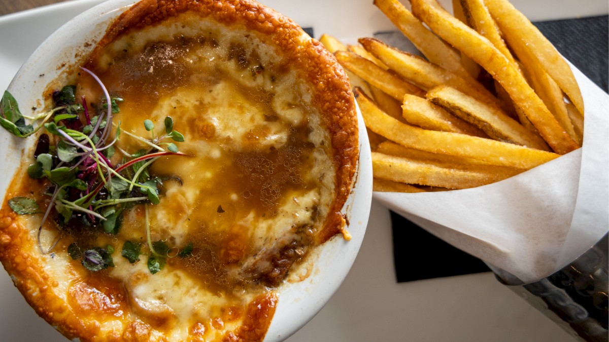 A cheesy baked dish (likely French onion soup topped) with a golden crust, served with a side of crunchy French fries.