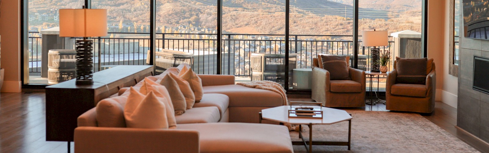 A spacious living room with large windows offering a mountain view, cozy furniture, and a warm ambiance with natural lighting.