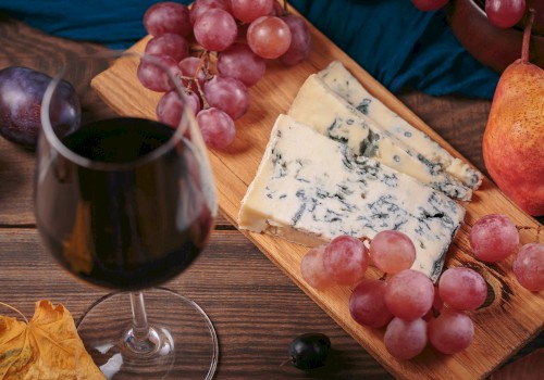 A glass of red wine, slices of blue cheese, grapes, pears, and plums on a wooden board create a cozy, inviting setting.