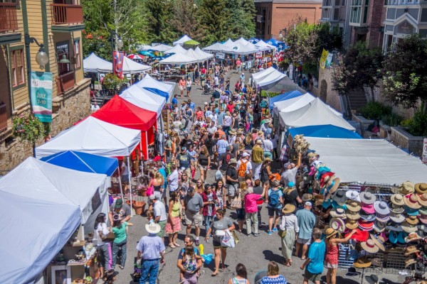 A busy outdoor market with numerous stalls and many people shopping on a sunny day.