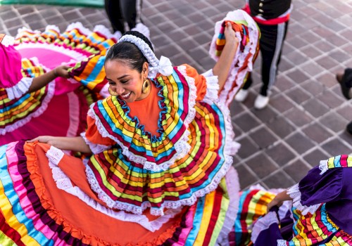 A person in a vibrant, colorful traditional dress is dancing joyfully on a tiled surface, surrounded by others in similar attire.