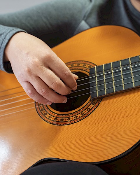 A person playing an acoustic guitar with their right hand strumming the strings and left hand on the fretboard, wearing a gray sleeve.
