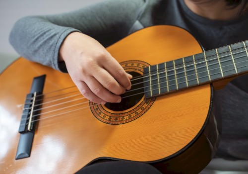 A person playing an acoustic guitar with their right hand strumming the strings and left hand on the fretboard, wearing a gray sleeve.