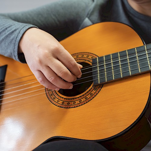 A person playing an acoustic guitar with their right hand strumming the strings and left hand on the fretboard, wearing a gray sleeve.