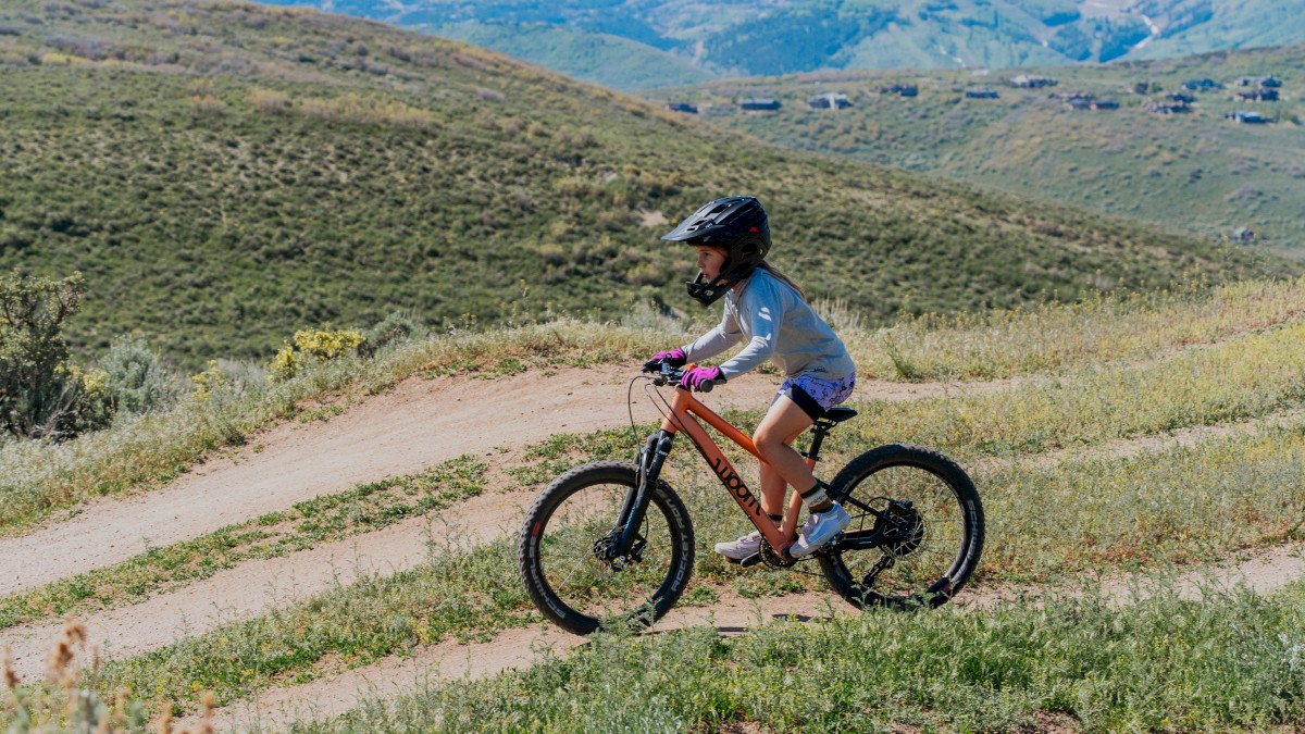 A person in a helmet rides a bicycle on a grassy trail with mountains in the background, enjoying an outdoor adventure.