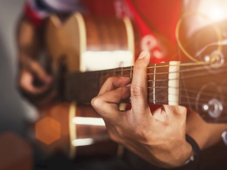 A person is playing an acoustic guitar, focused on the fretboard, with a warm light creating a cozy atmosphere in the scene.