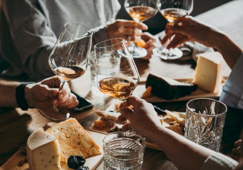 People clinking wine glasses over a table with assortments of cheese and snacks, creating a cozy and celebratory atmosphere.
