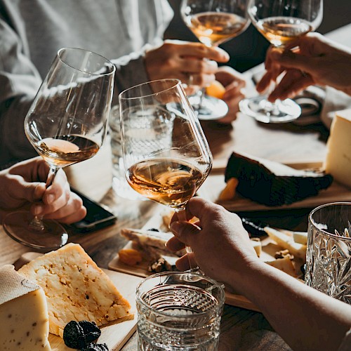 People clinking wine glasses over a table with assortments of cheese and snacks, creating a cozy and celebratory atmosphere.
