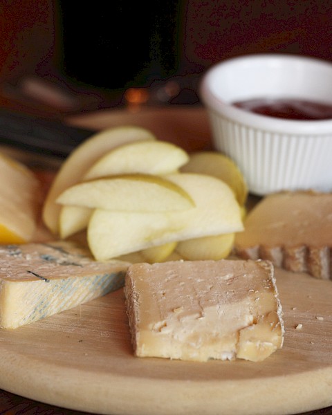 A cheese platter with apple slices, various cheeses, and a small dish of jam on a wooden board.