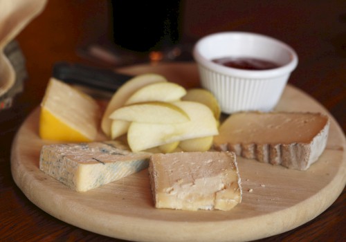 A cheese platter with apple slices, various cheeses, and a small dish of jam on a wooden board.