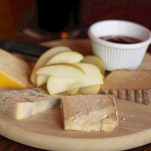A cheese platter with apple slices, various cheeses, and a small dish of jam on a wooden board.