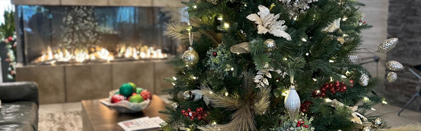 A decorated Christmas tree with lights and ornaments in a cozy living room setting featuring a modern fireplace and contemporary furniture.