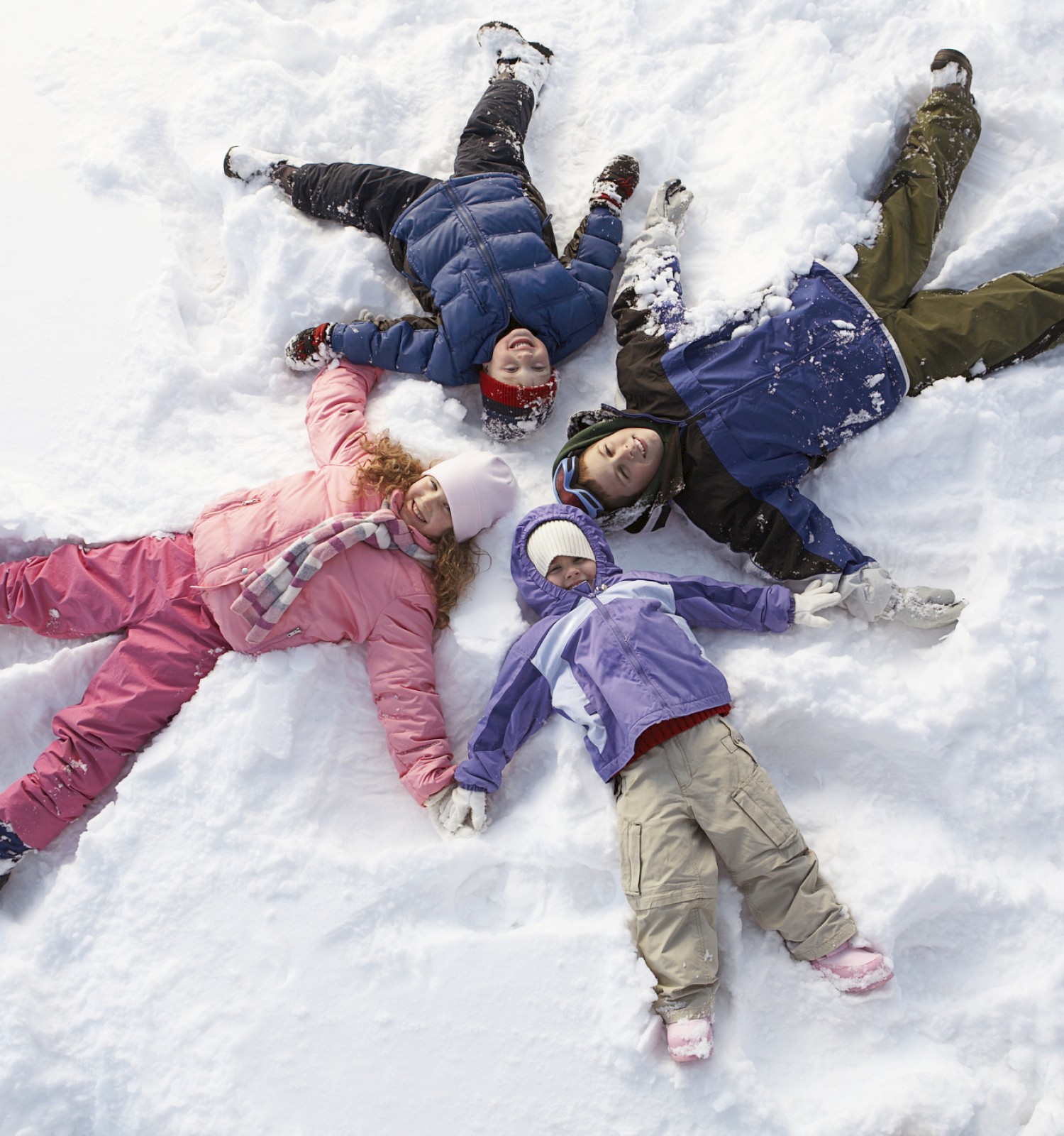 A family of five is lying on the snow in a star-shaped formation, enjoying winter together.