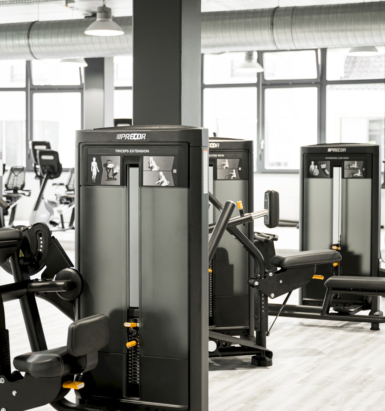 A modern gym with various exercise machines arranged neatly in a spacious, well-lit room with large windows and a sleek design.