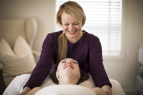 A woman is giving a massage to another person who is lying down and appears relaxed, in a softly lit room.