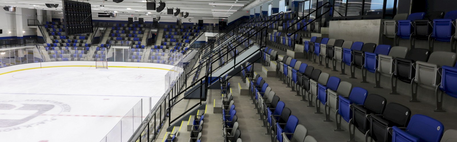 An empty hockey arena with seats in blue, black, and gray around an ice rink, ready for a game in a modern indoor stadium.
