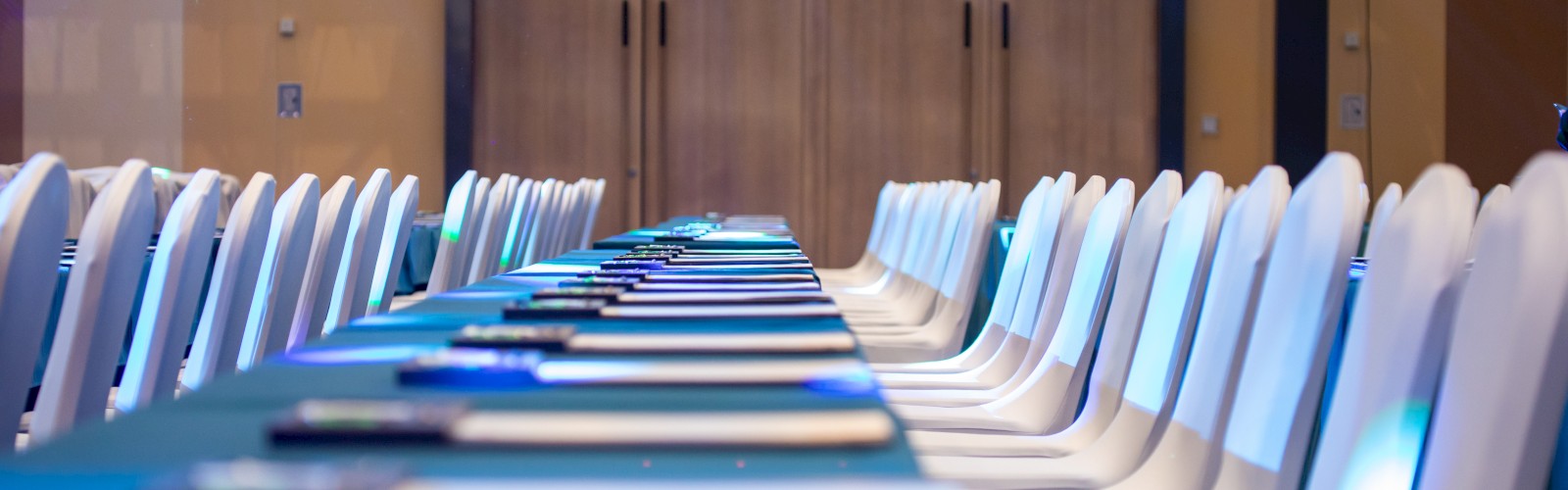 A long table with neatly arranged white chairs set for a conference or meeting, with notepads and pens on the table.