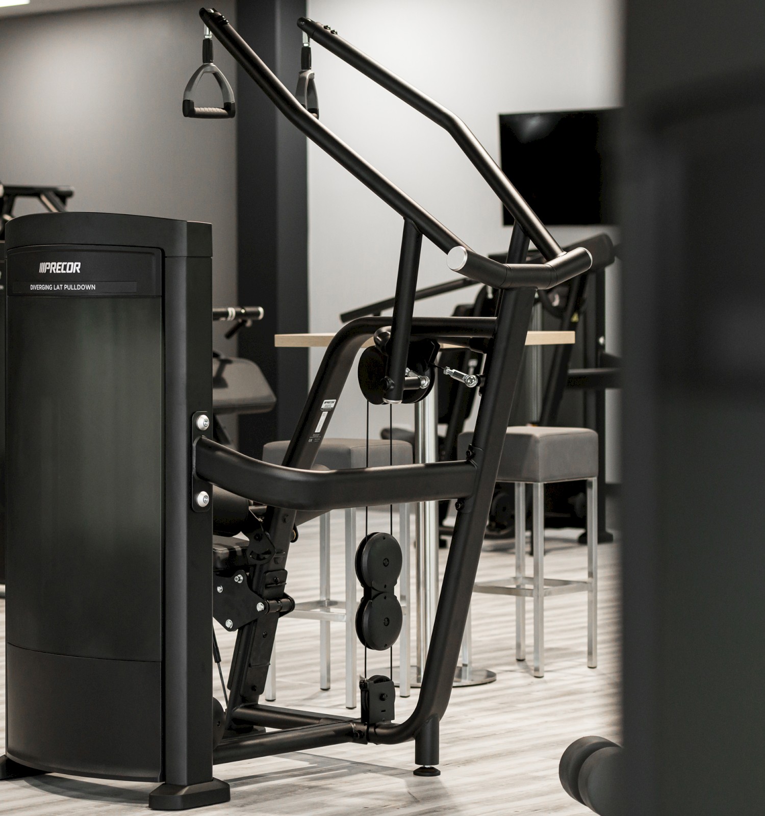 The image shows gym equipment in a fitness center setting, featuring a weight machine positioned prominently in the foreground.