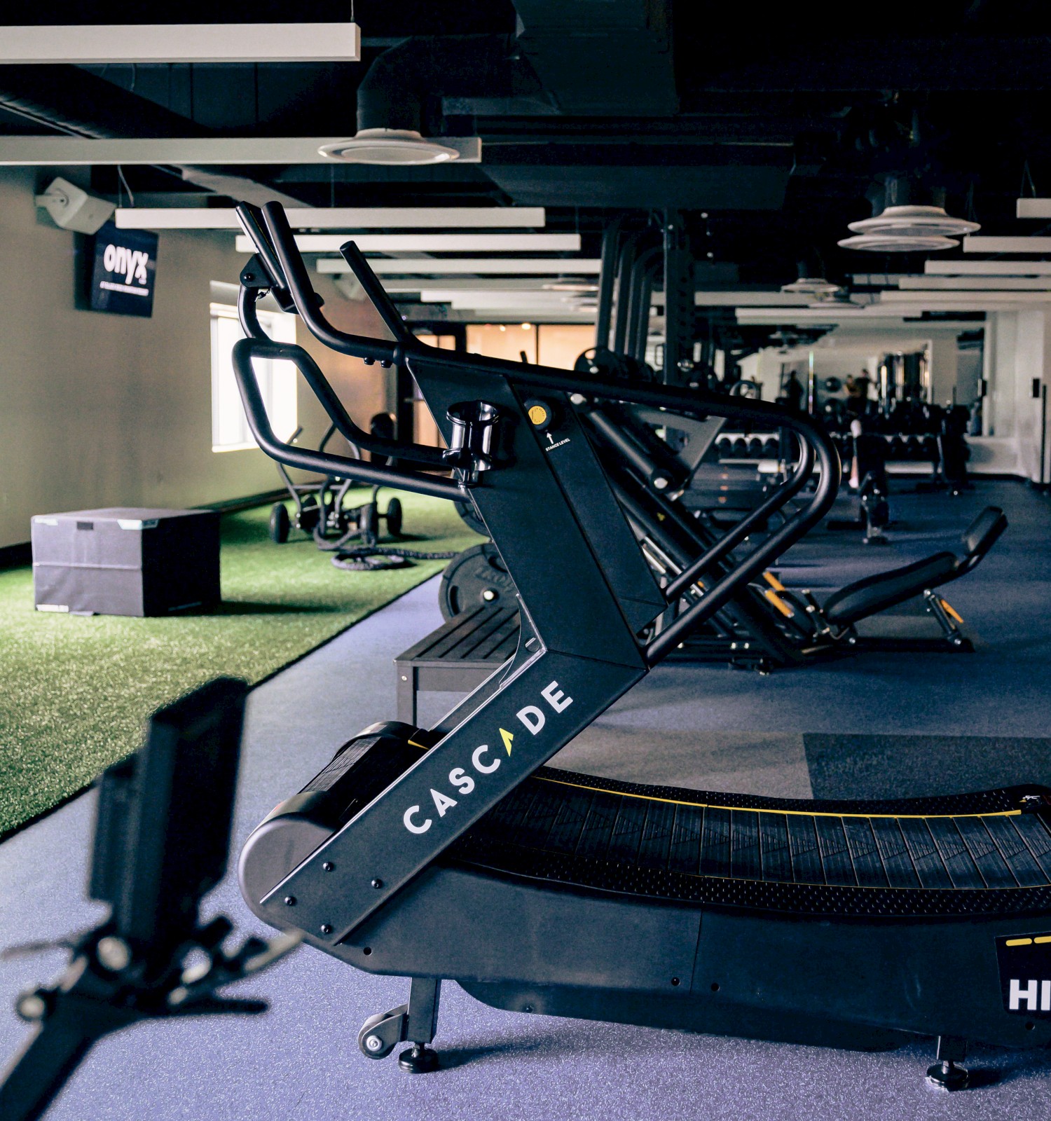 An empty fitness studio with various workout equipment, including a curved treadmill, machines, and a small grassy area.